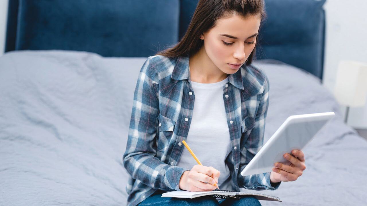 Woman holding digital tablet and writing in notebook